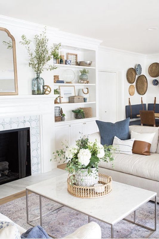 Bright white living room with fireplace, built-in shelves, beige sofa, coffee table, and floral centerpiece