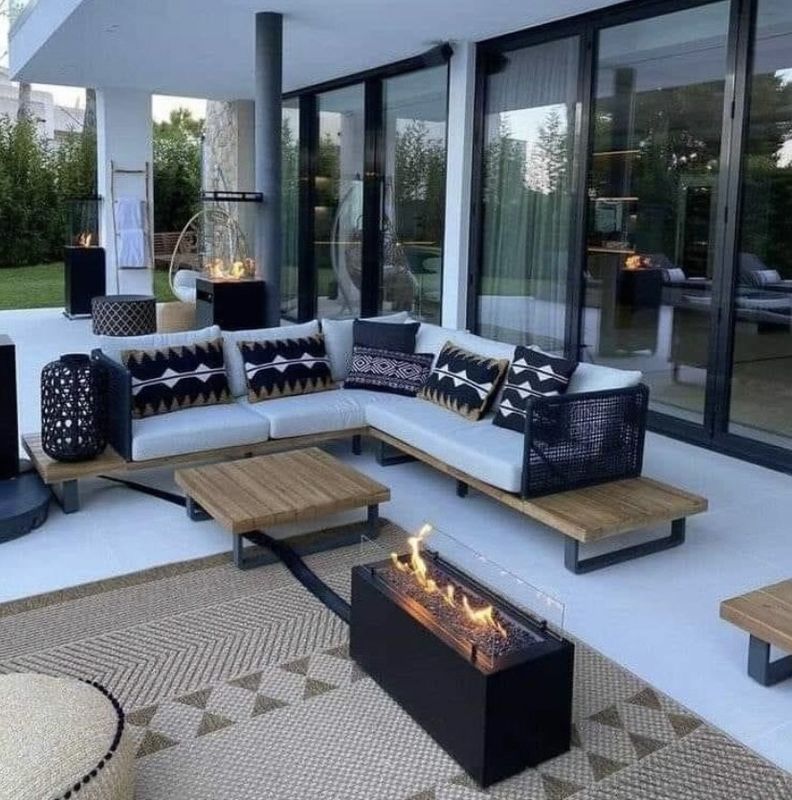Modern patio with white sectional sofa, fire pit, rug, and glass doors overlooking a garden