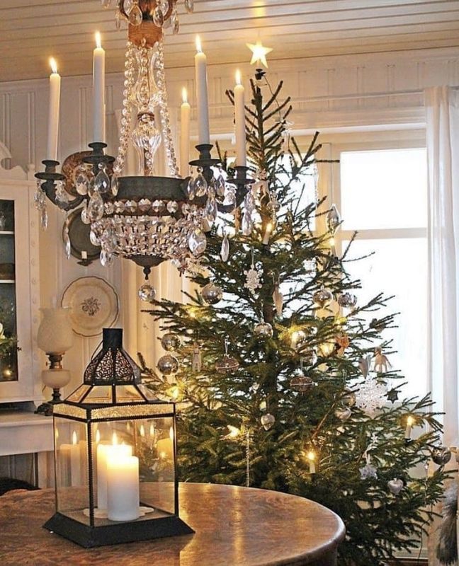 Cozy dining room with a lit Christmas tree, chandelier, candles, and lantern on a table