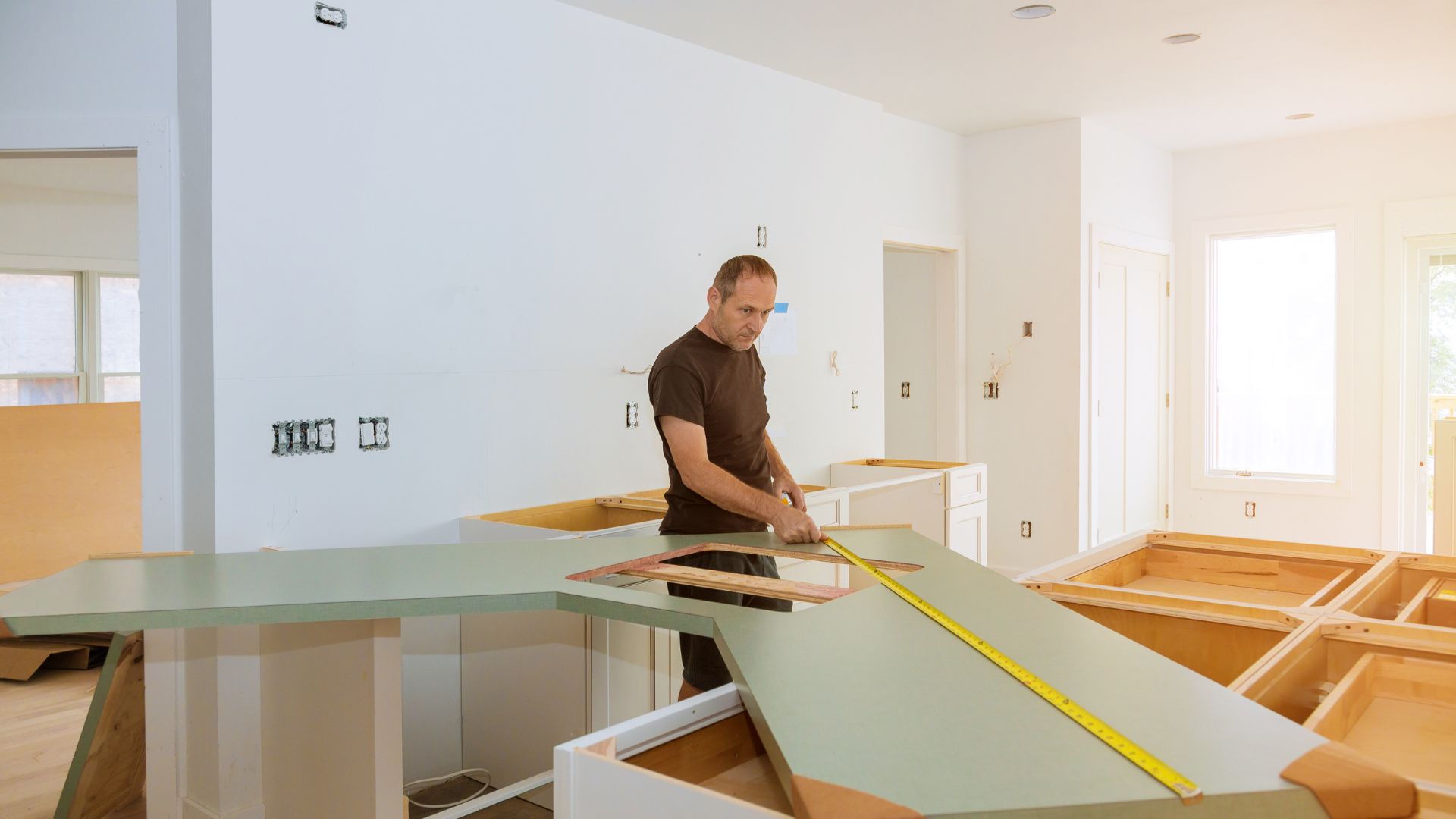 Worker measuring a countertop in a bright kitchen under renovation