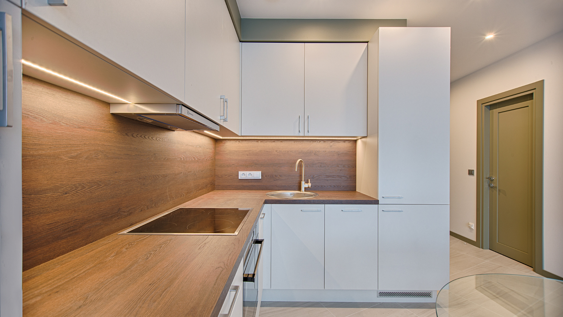 Modern kitchen with light wood countertops, white cabinets, copper backsplash, sink, and tall pantry cabinet