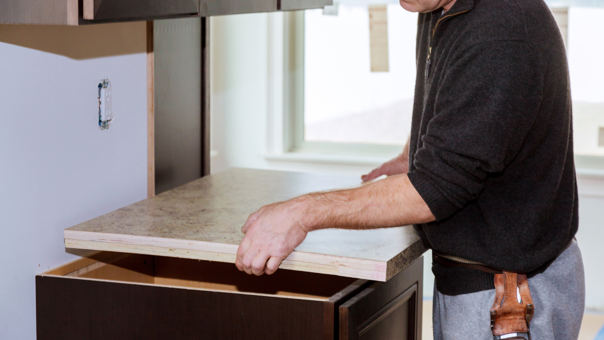 Person sliding a stone countertop slab into place in a kitchen renovation.