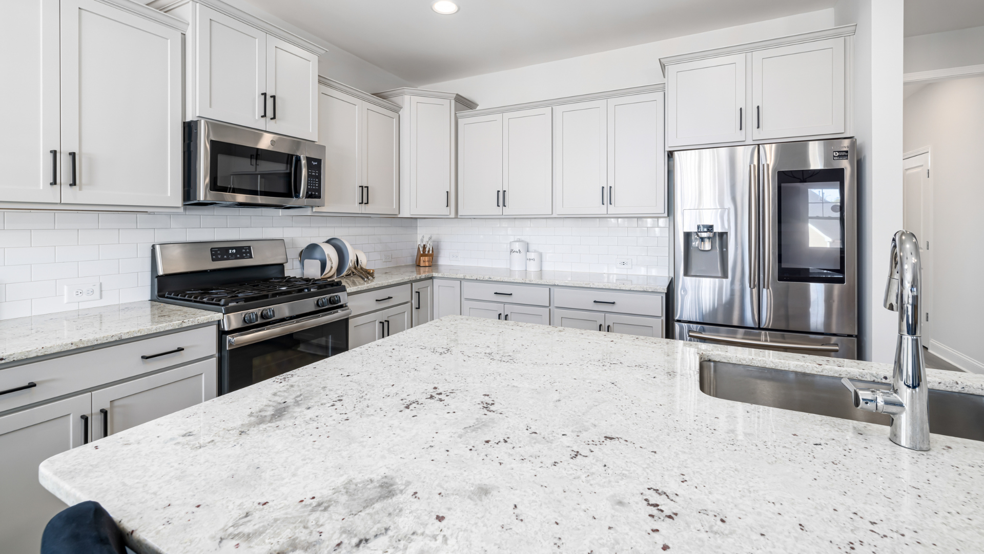 A kitchen with white cabinets , stainless steel appliances , and granite counter tops.