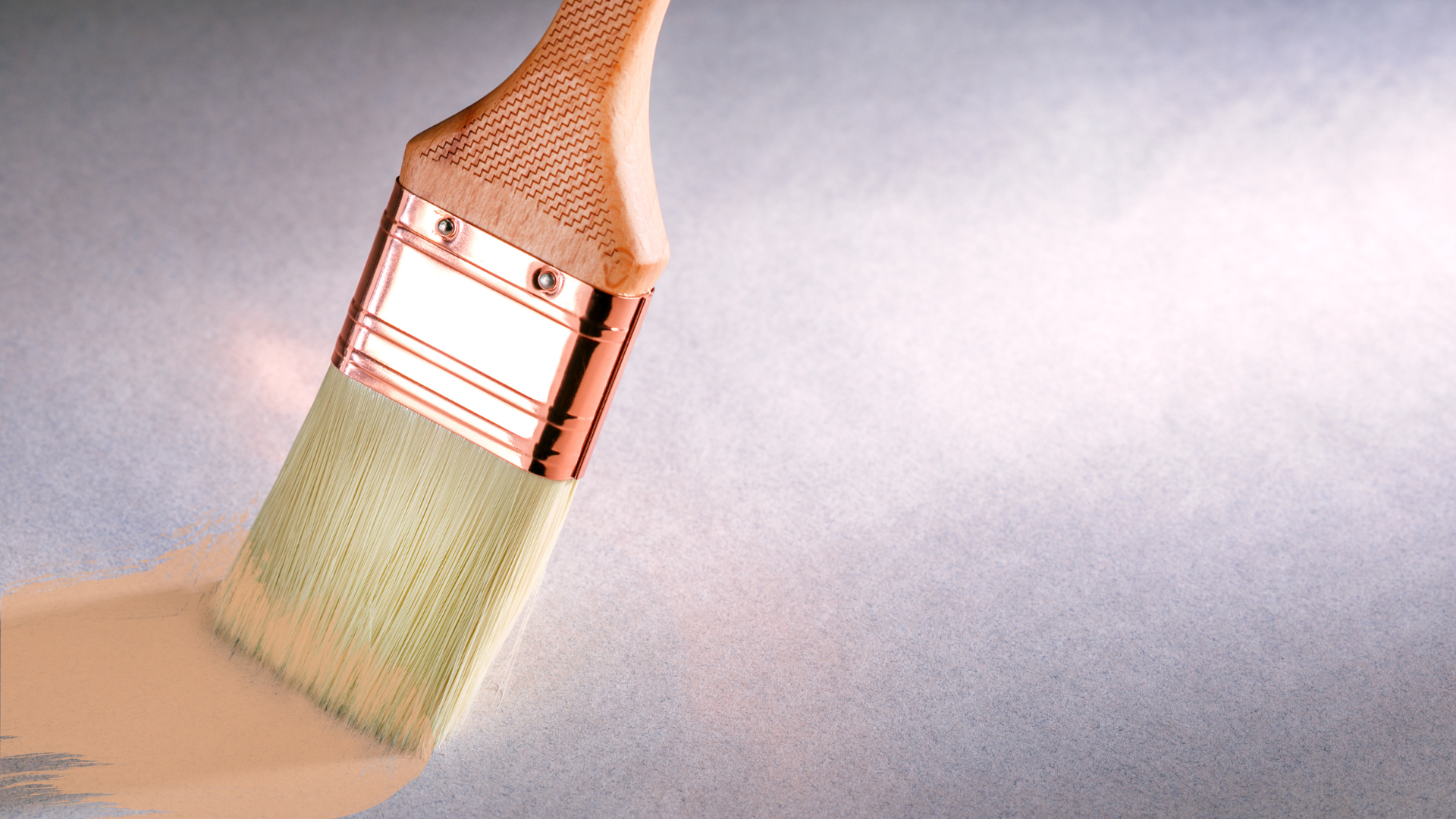 Paintbrush applying white paint in a smooth diagonal stroke on a light surface