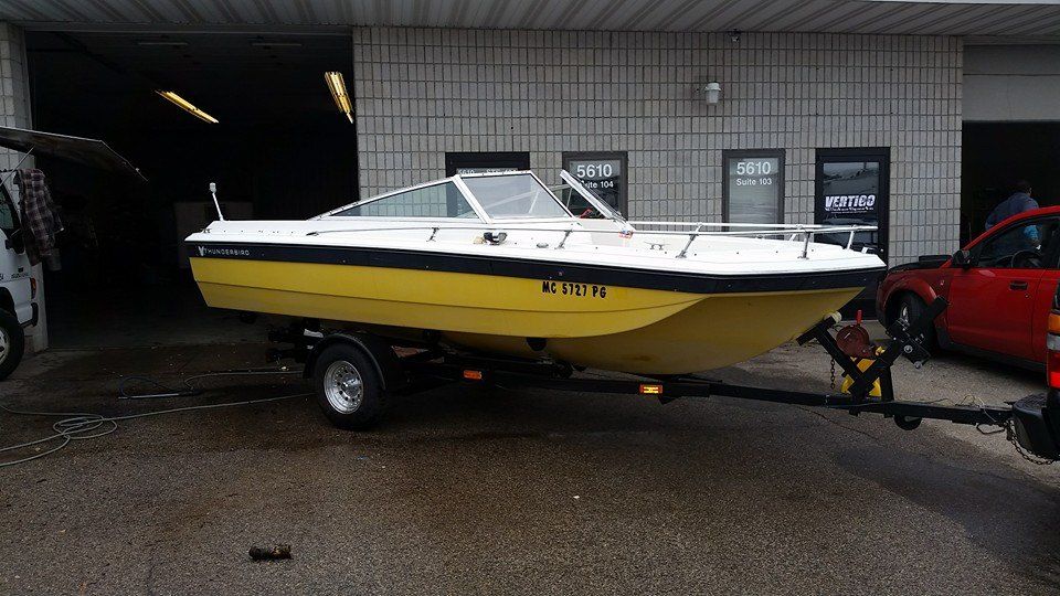 A yellow and white boat is on a trailer in front of a building.