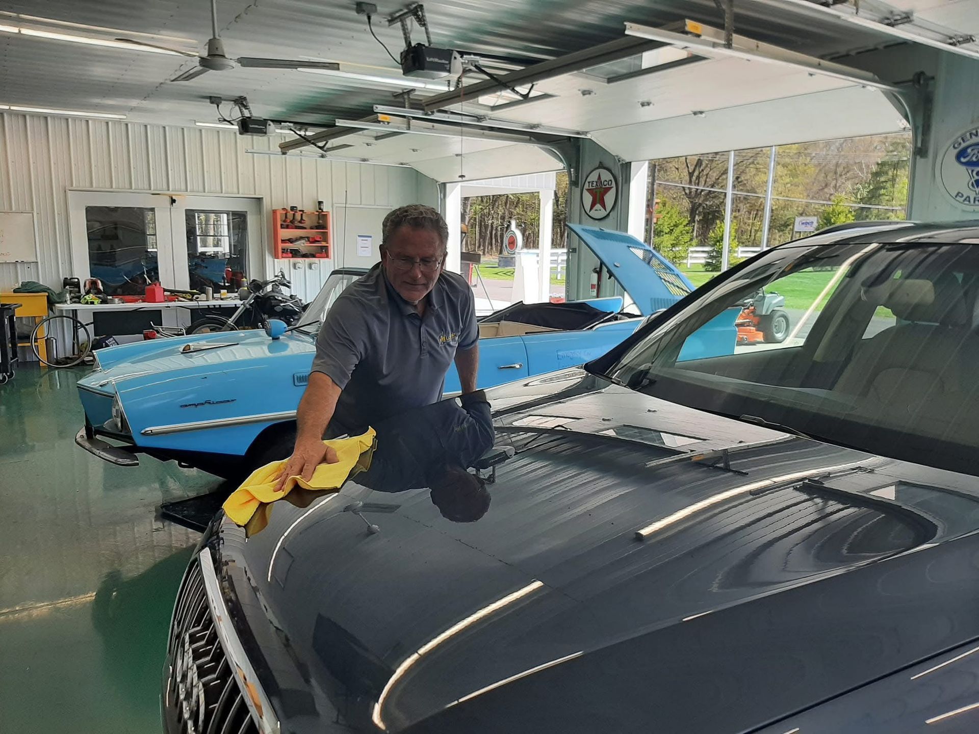 A man is cleaning the hood of a car in a garage.