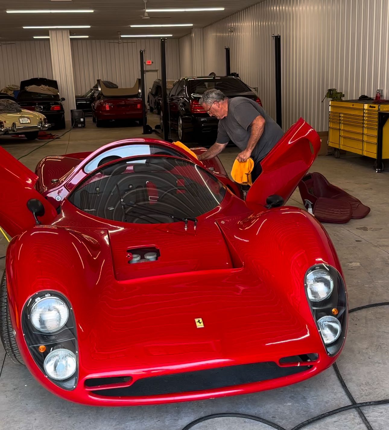 A man is cleaning a red sports car in a garage