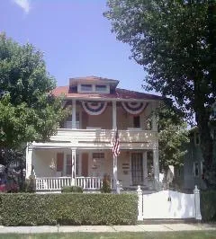 A two-story house with a white front porch and balcony, adorned with patriotic bunting and an American flag.