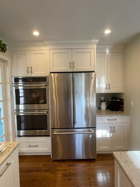 A kitchen featuring white cabinetry, a built-in double oven, a stainless steel refrigerator, and granite countertops.