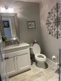 A small bathroom featuring a white vanity with a silver-framed mirror, a toilet, and wall art in a gray-toned space.