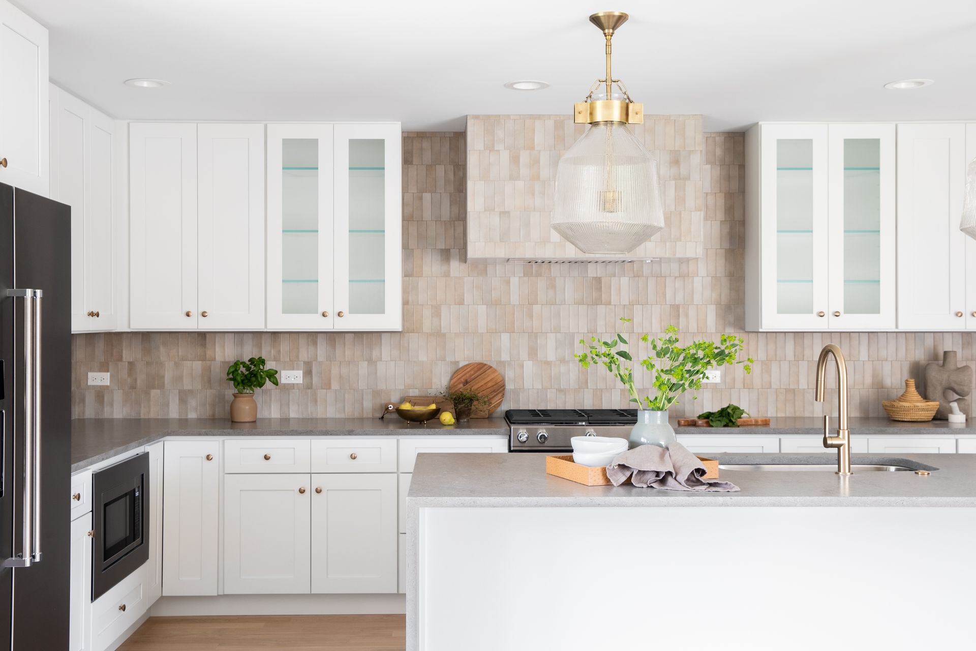 A bright, modern kitchen features white cabinetry, a light-toned textured backsplash, a kitchen island, and a pendant light.