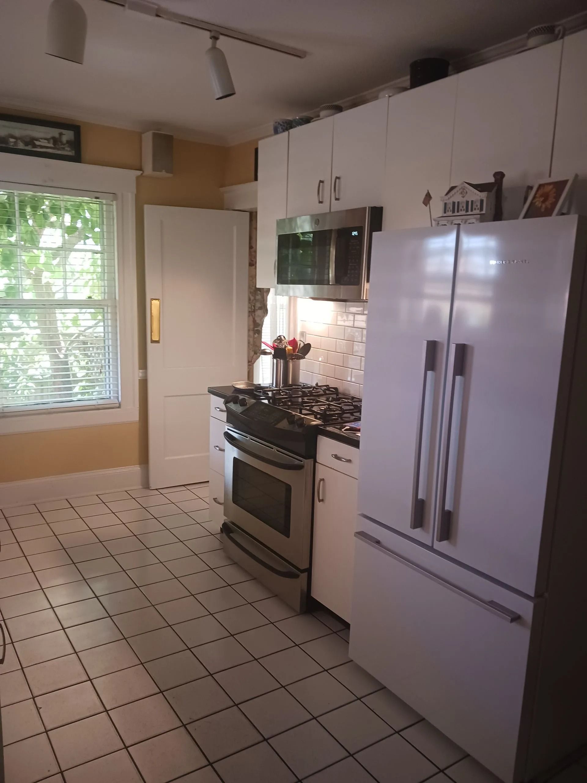 A kitchen with white cabinets, a stainless steel gas range and microwave, a white refrigerator, and white-tiled floors.