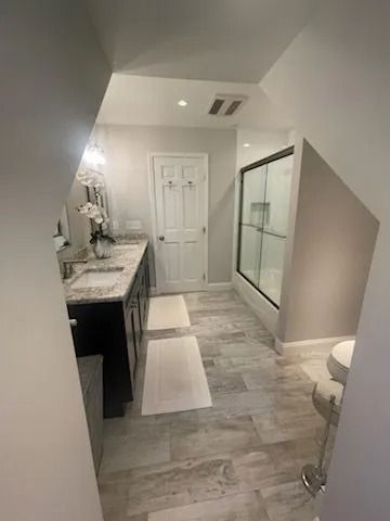 Modern bathroom with a marble-topped vanity, grey cabinets, glass shower enclosure, and light-toned tile flooring.