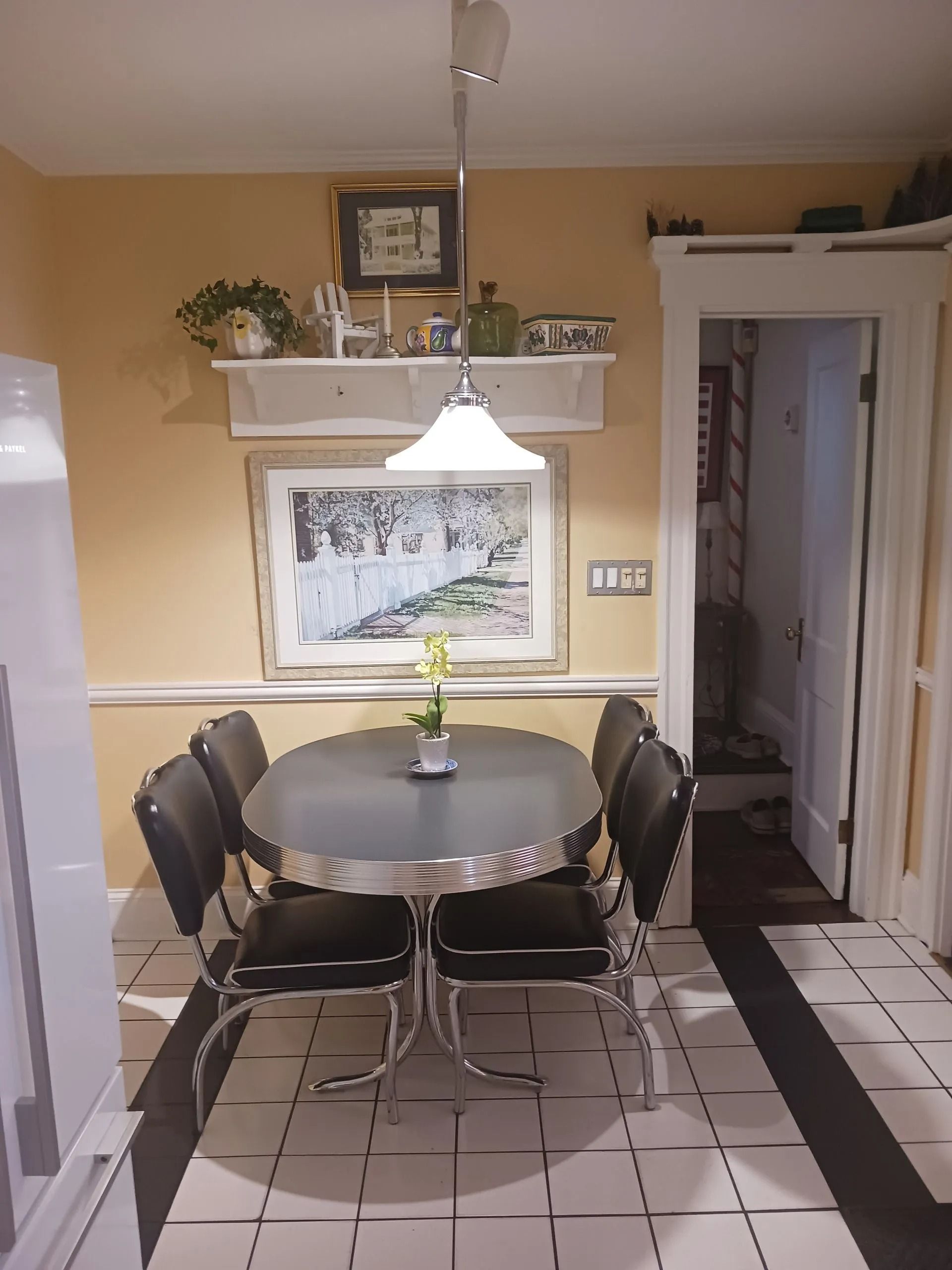 A retro dining set with an oval table and four black chairs under a pendant light in a yellow-walled dining area.