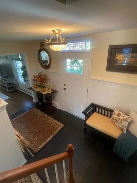 An entryway seen from stairs, featuring a rug, a wooden table with decor, a bench with pillows, and a white front door.