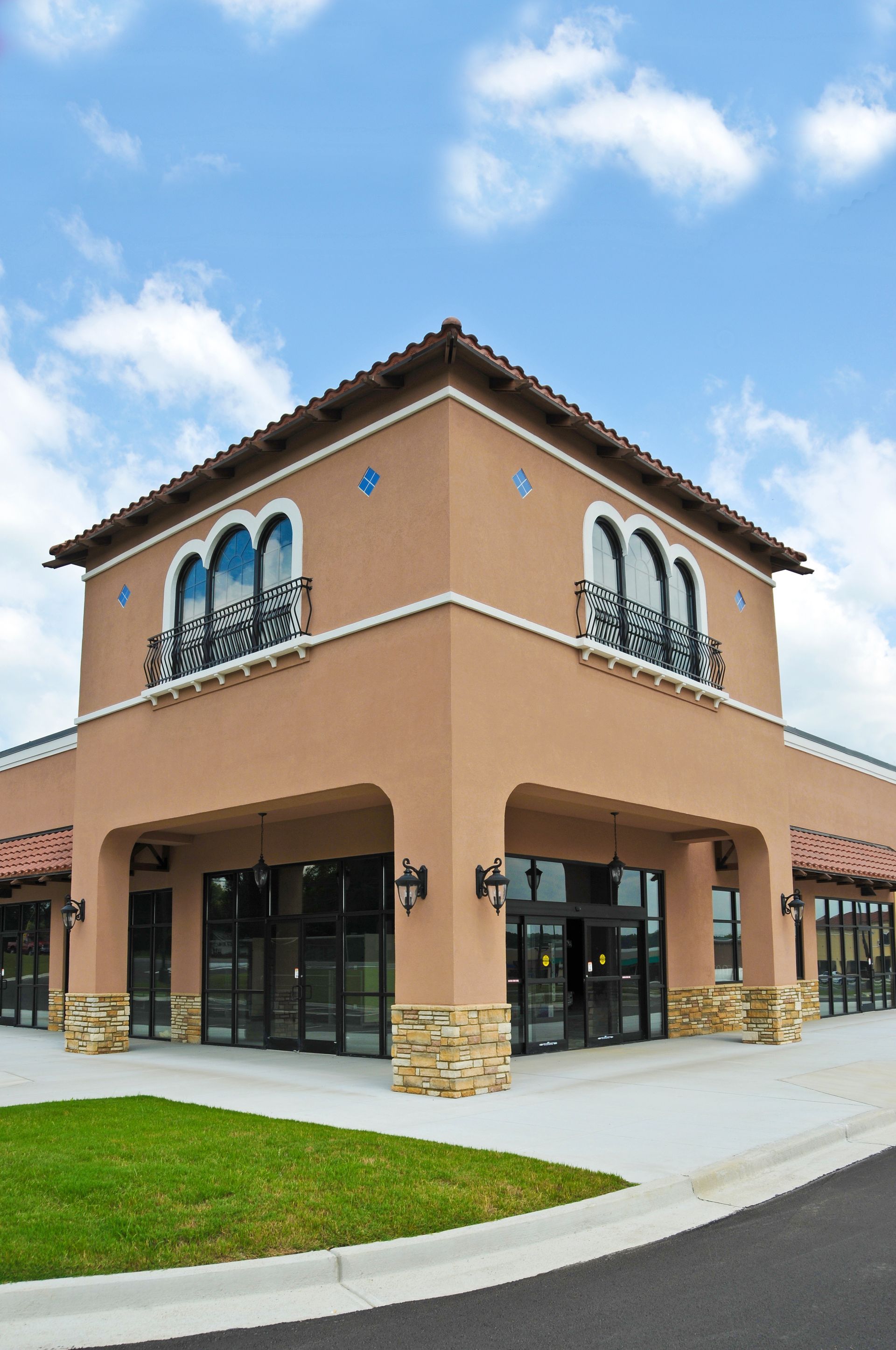 Corner view of a tan, stucco commercial building with arched windows, stone accents, and glass storefronts.
