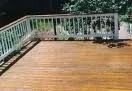 A wooden deck with a white railing overlooks a shaded yard with trees.