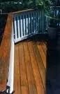 A wooden deck with a corner staircase, featuring a stained brown surface and a white railing with vertical balusters.
