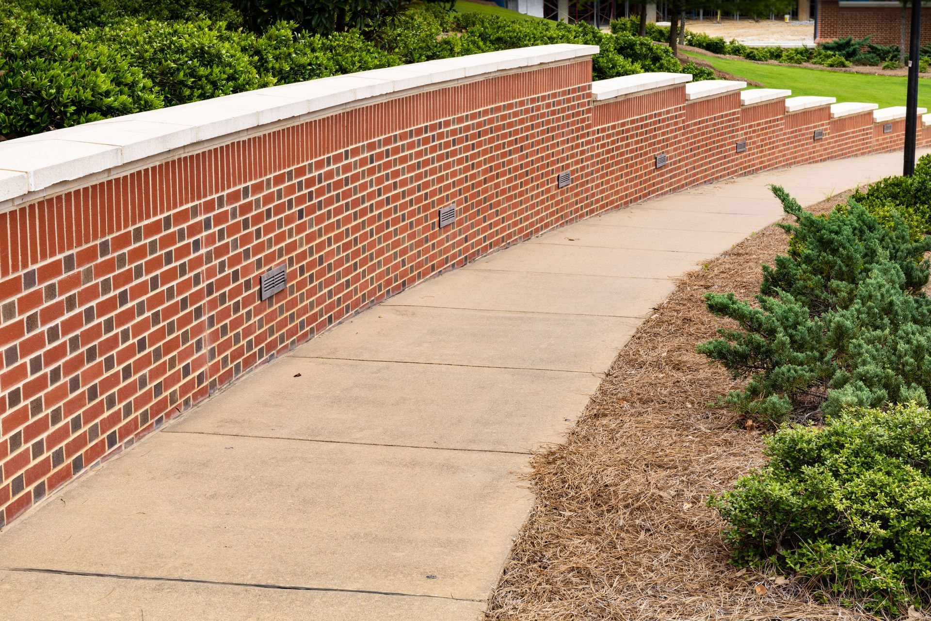 A curved brick retaining wall with inset lights runs alongside a concrete sidewalk and landscaped garden.