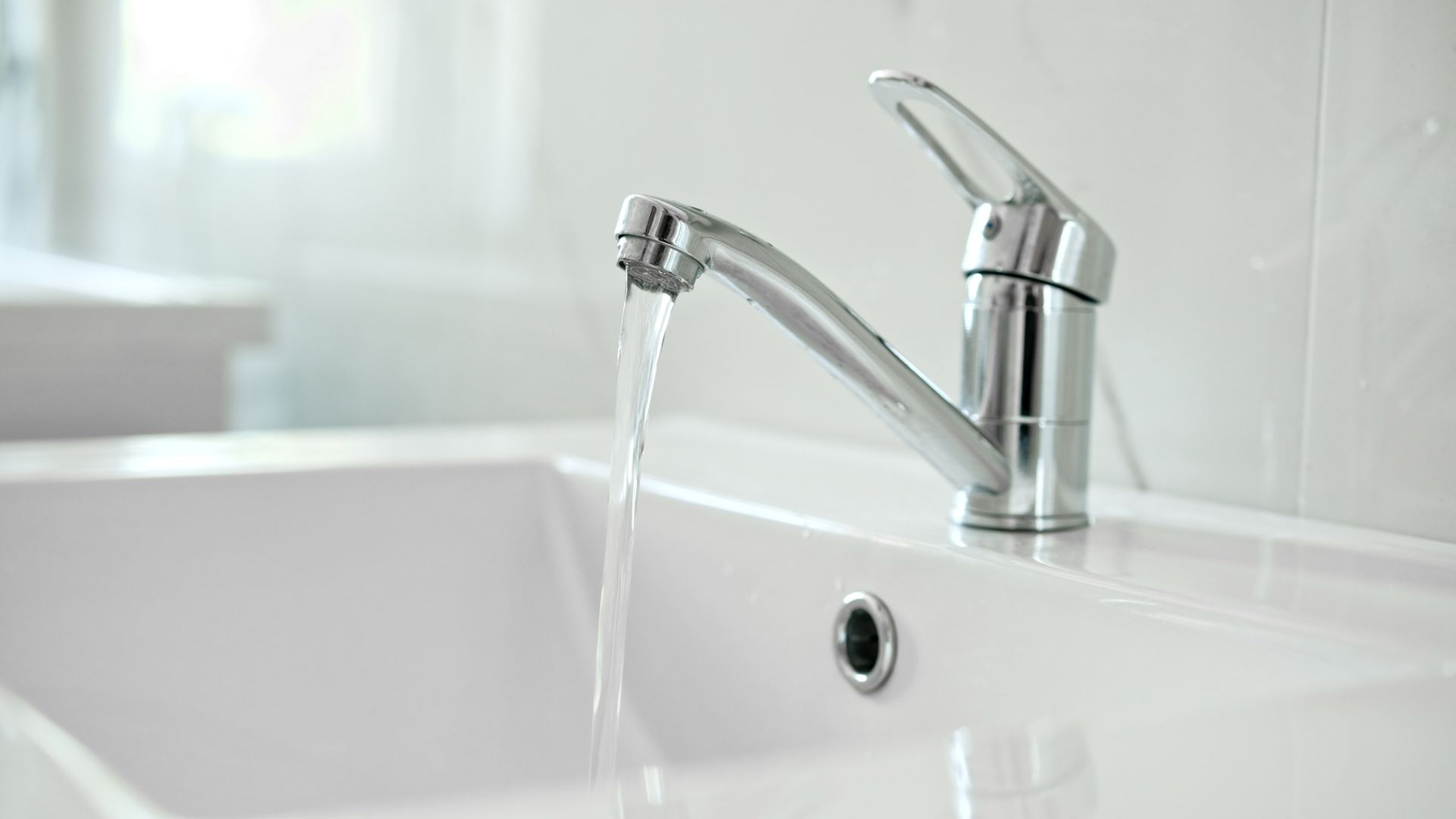 A chrome faucet flows into a white bathroom sink.