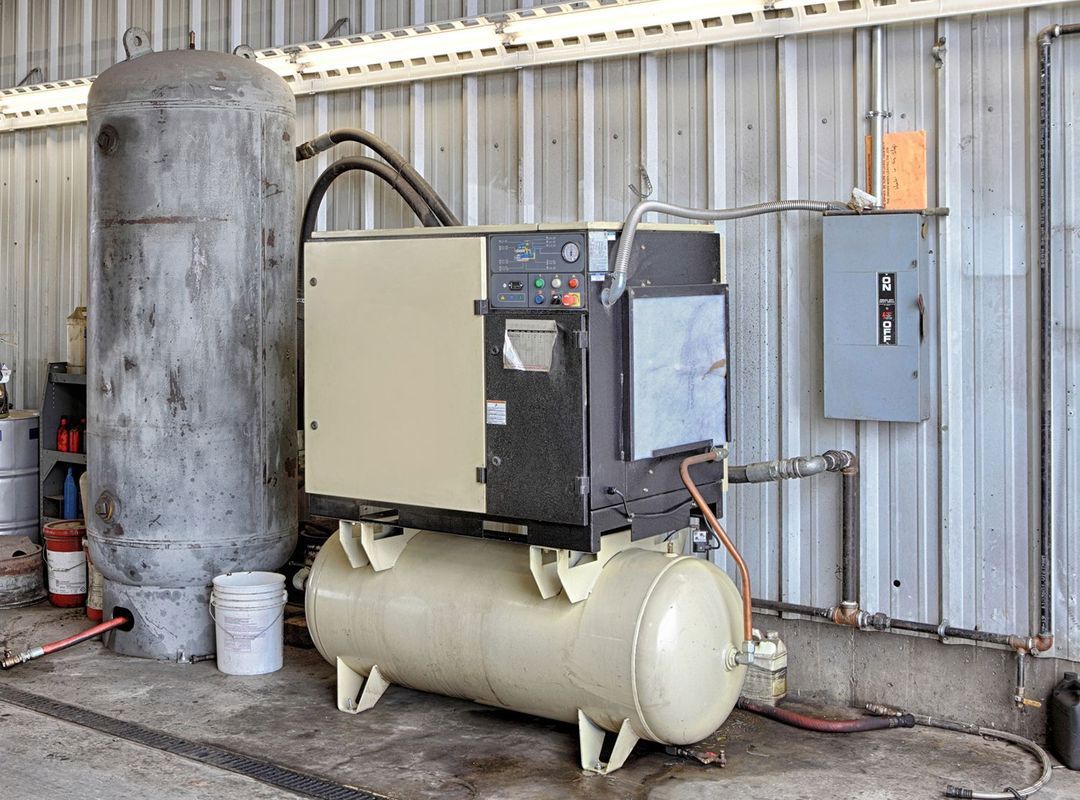 A large air compressor is sitting next to a large tank in a warehouse.