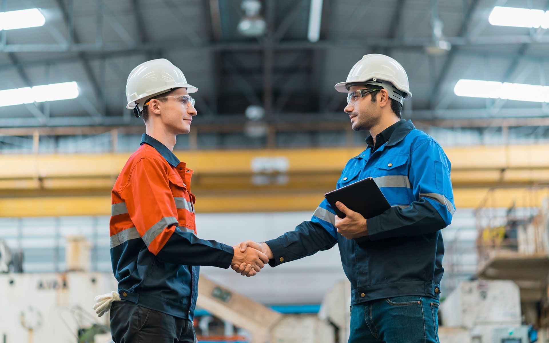 Two construction workers are shaking hands in a factory.