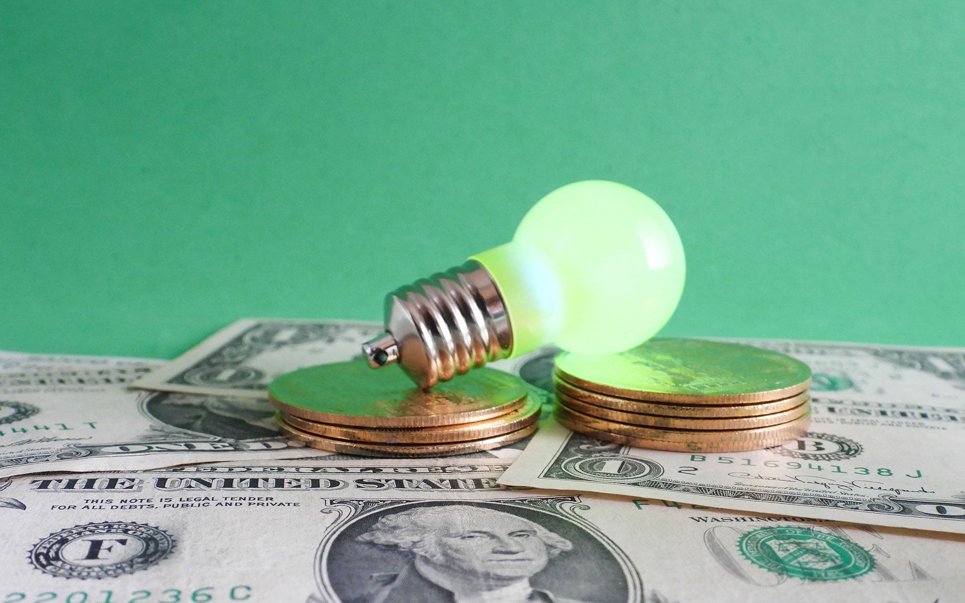 A light bulb is sitting on top of a pile of coins and money.