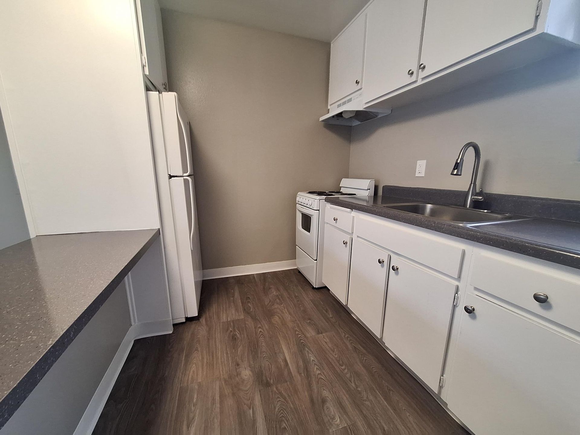 A kitchen with white cabinets , a refrigerator , stove , sink and counter.