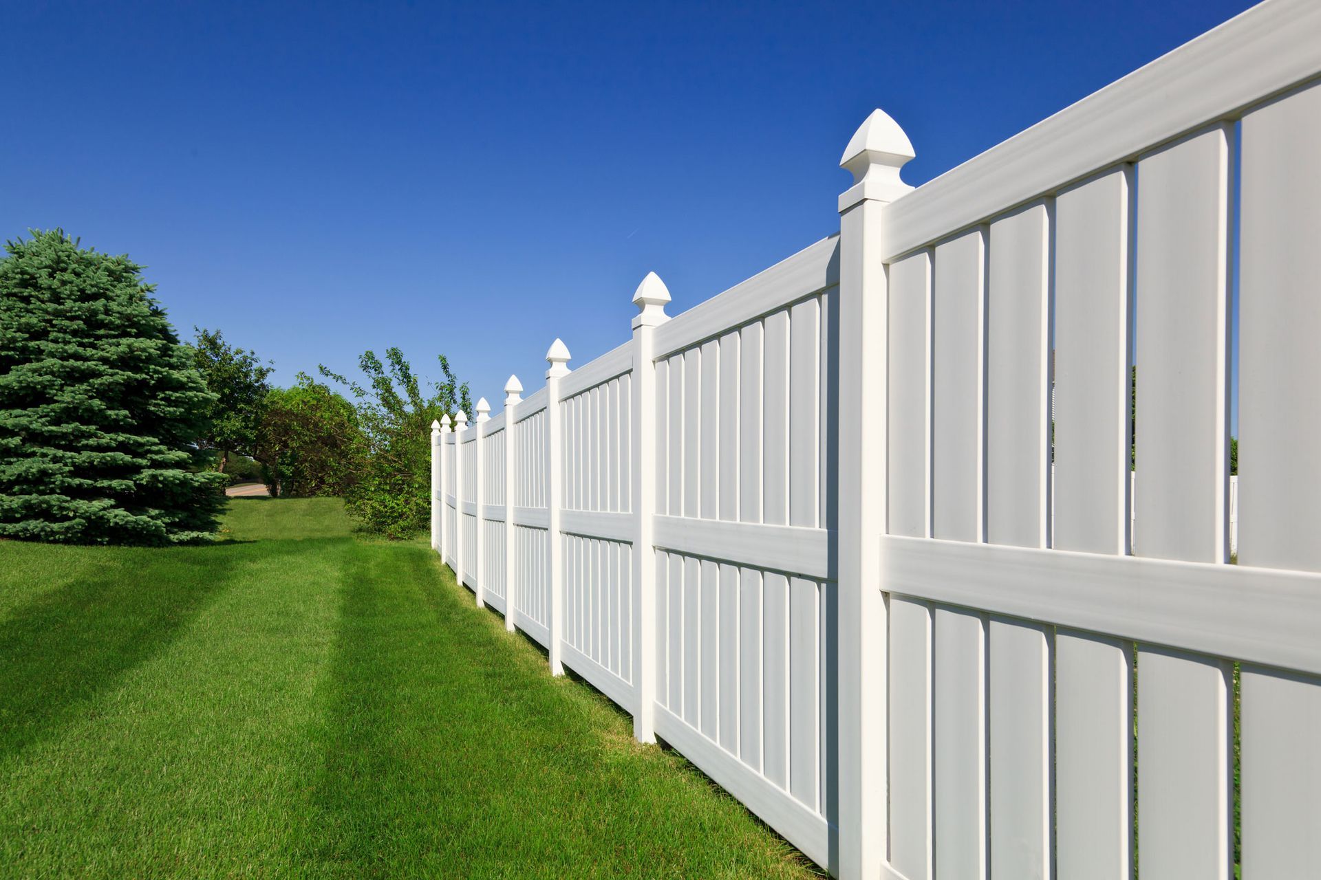 White vinyl fence along a green lawn under a bright blue sky.