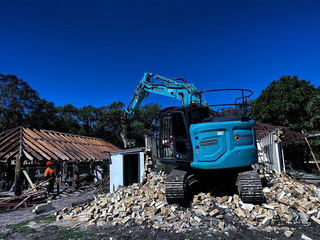 A Blue Excavator Is Demolishing a Building in A Field — Northern Rivers Demolition & Asbestos in Grafton, NSW