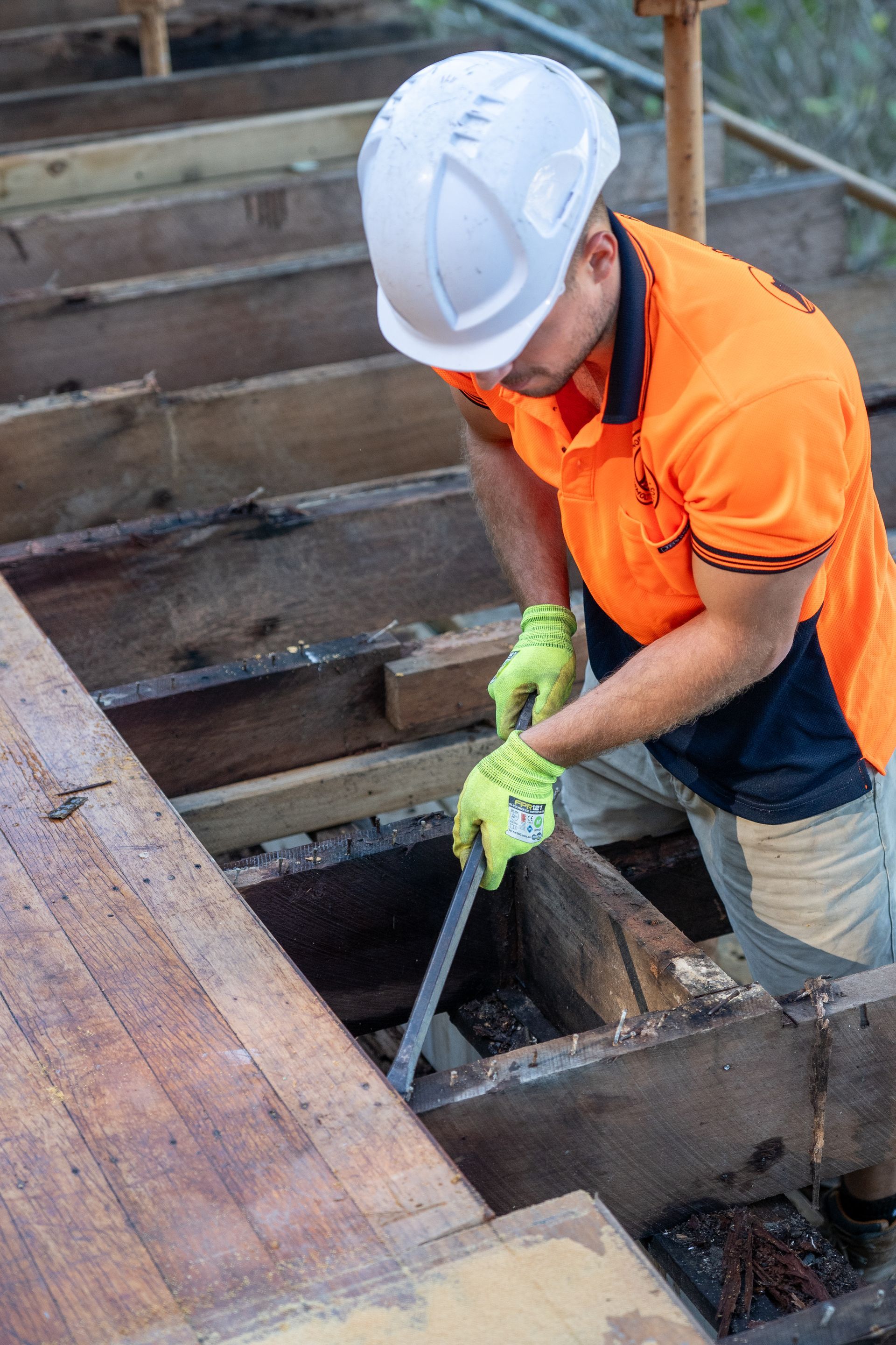 A man wearing a hard hat and orange shirt is working on a wooden floor.