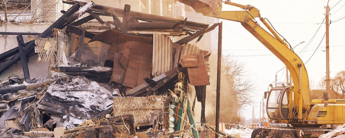 A Yellow Excavator Is Demolishing a Building — Northern Rivers Demolition & Asbestos in Skennars Head, NSW A Yellow Excavator Is Demolishing a Building — Northern Rivers Demolition & Asbestos in Skennars Head, NSW
