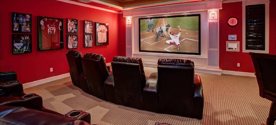 home theater with baseball on the large format screen, red walls, and plush luxury recliners.