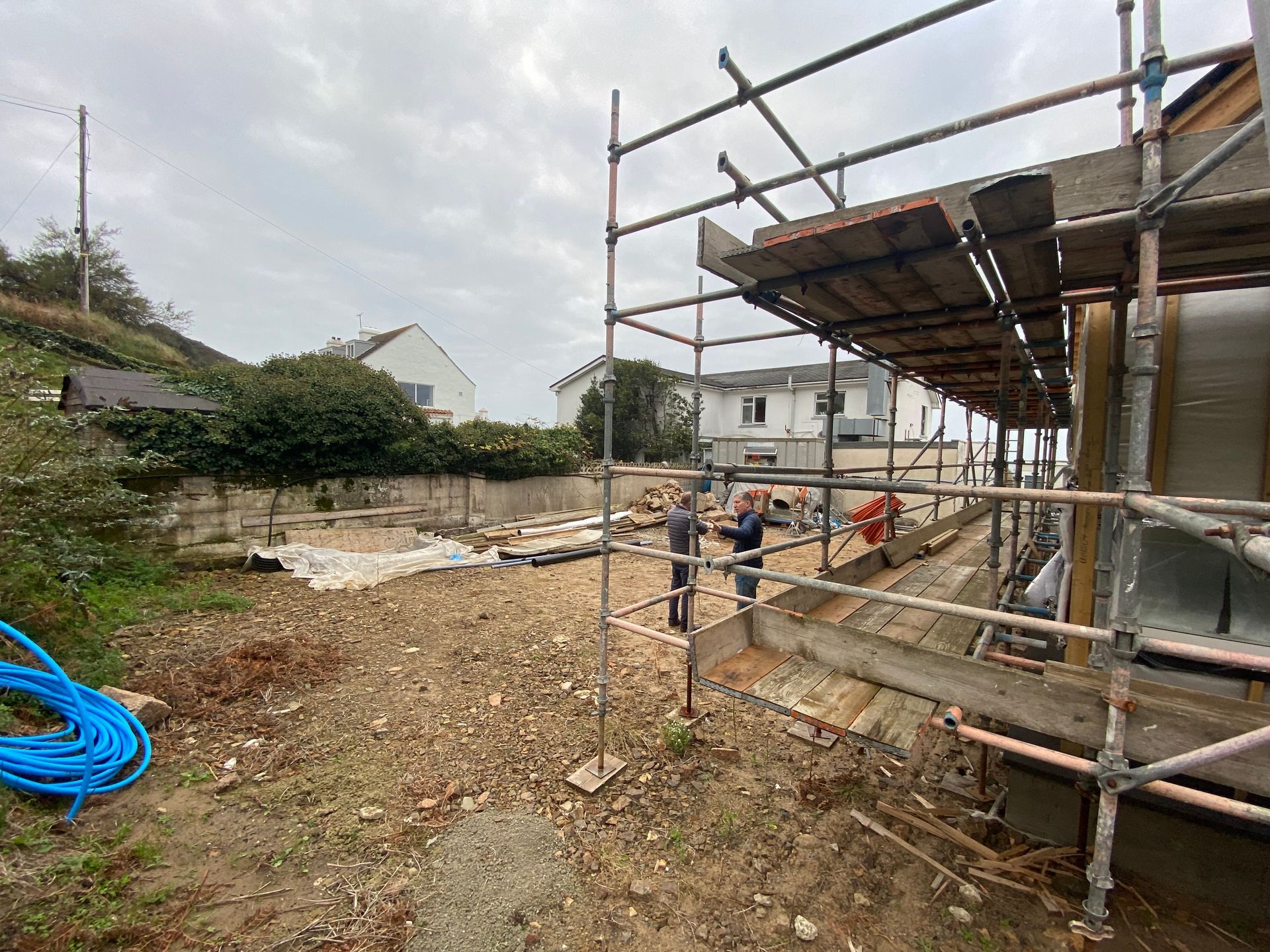 Construction site with scaffolding. Workers are visible near a partially built structure, surrounded by earth and equipment.