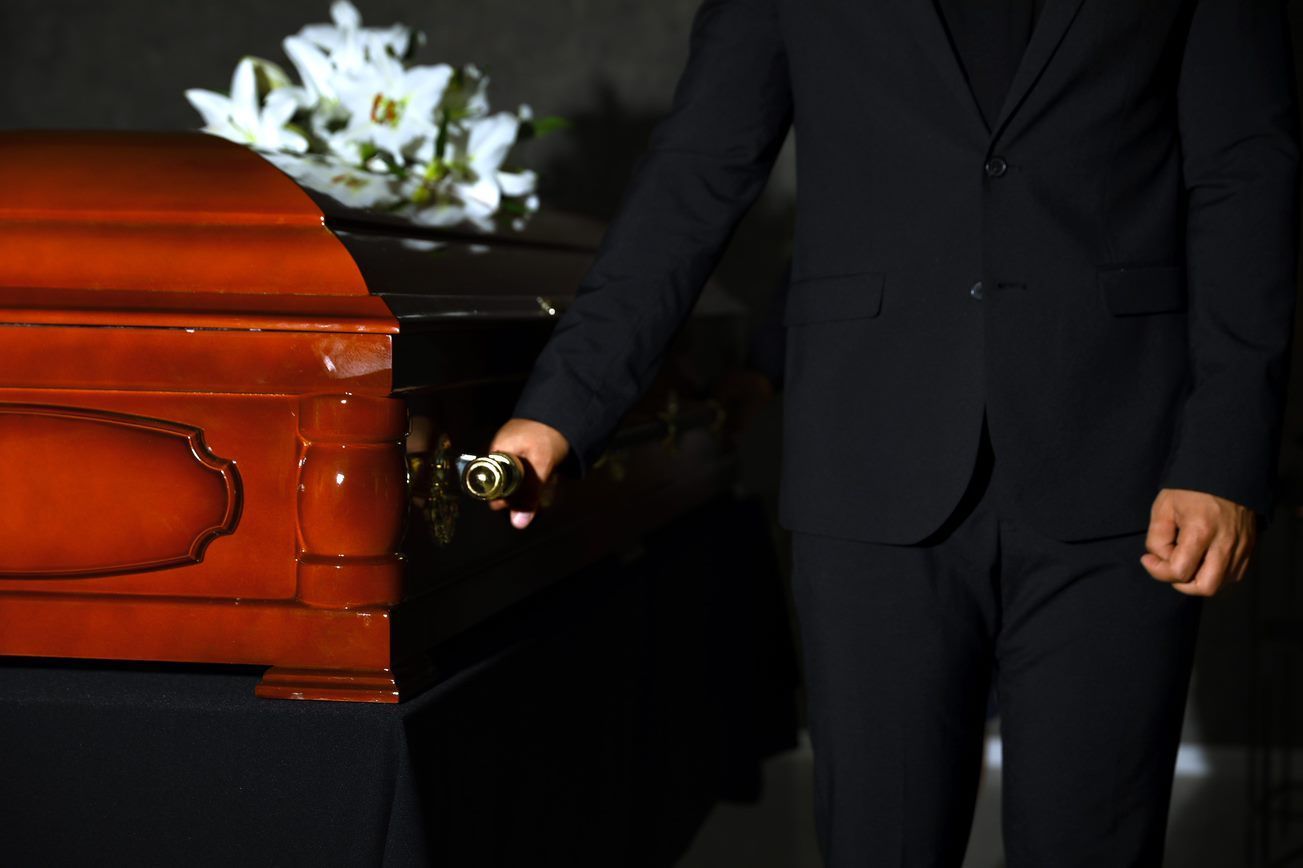 a man in a suit is opening a coffin at a funeral .