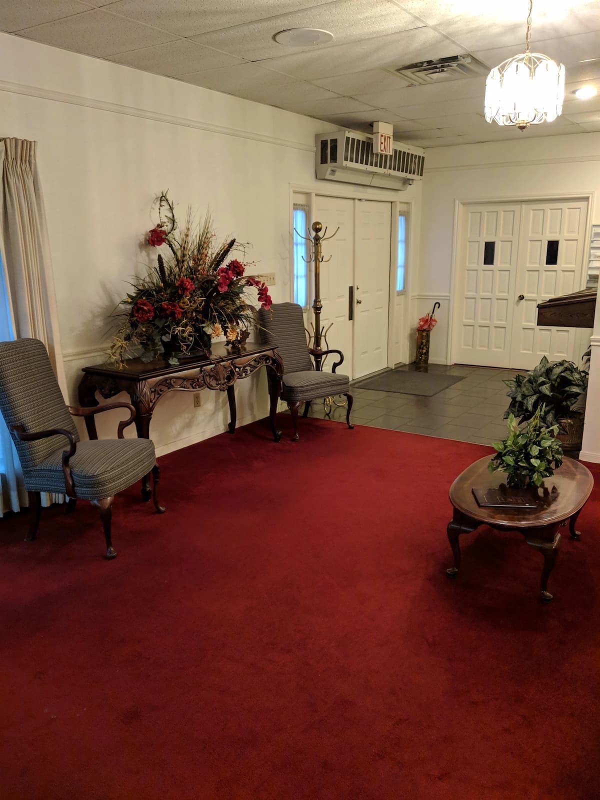 a living room with red carpet , chairs , a table and a vase of flowers .
