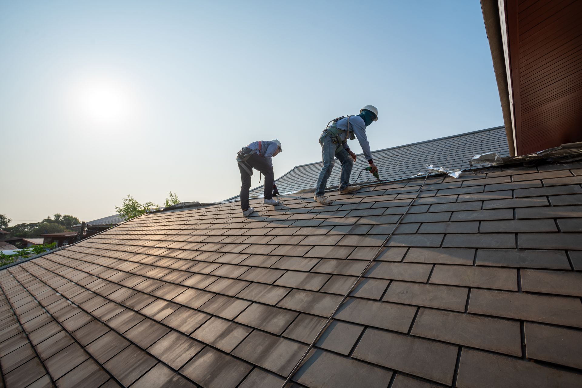 Two roofers install tile shingles on a commercial roof at sunset.