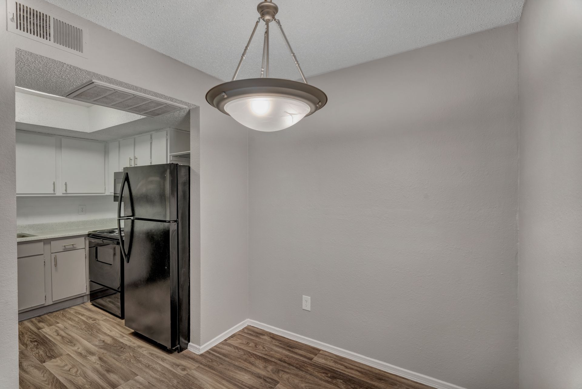 An empty dining room with a black refrigerator and a chandelier.
