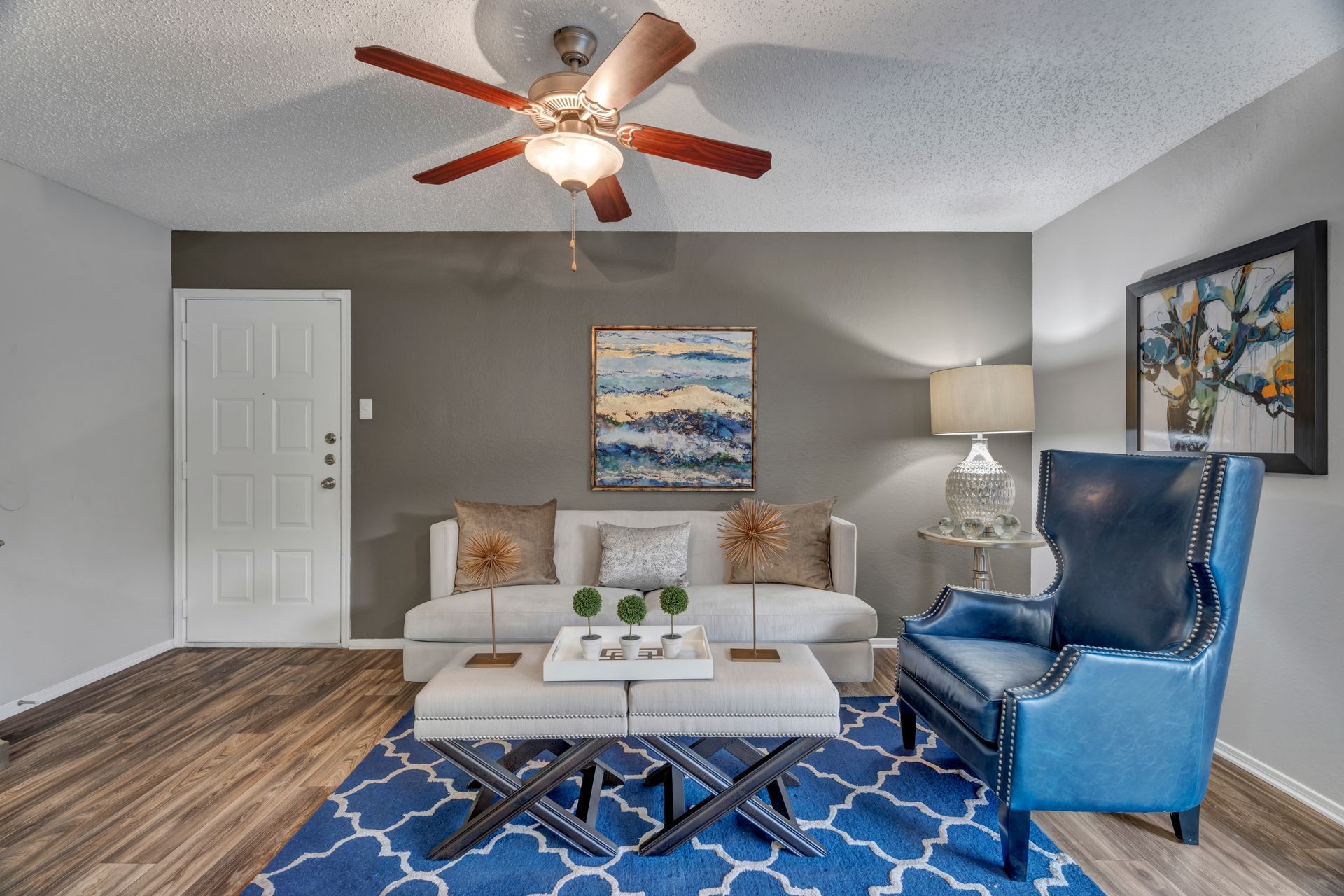A living room with a couch , chair , coffee table and ceiling fan.
