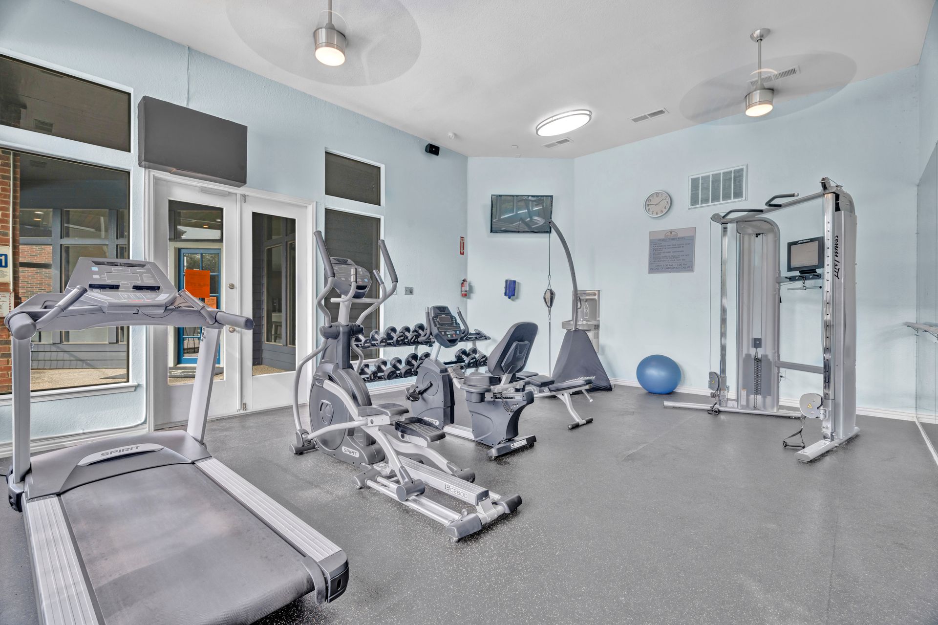 A gym with a treadmill , elliptical , dumbbells , and other exercise equipment.