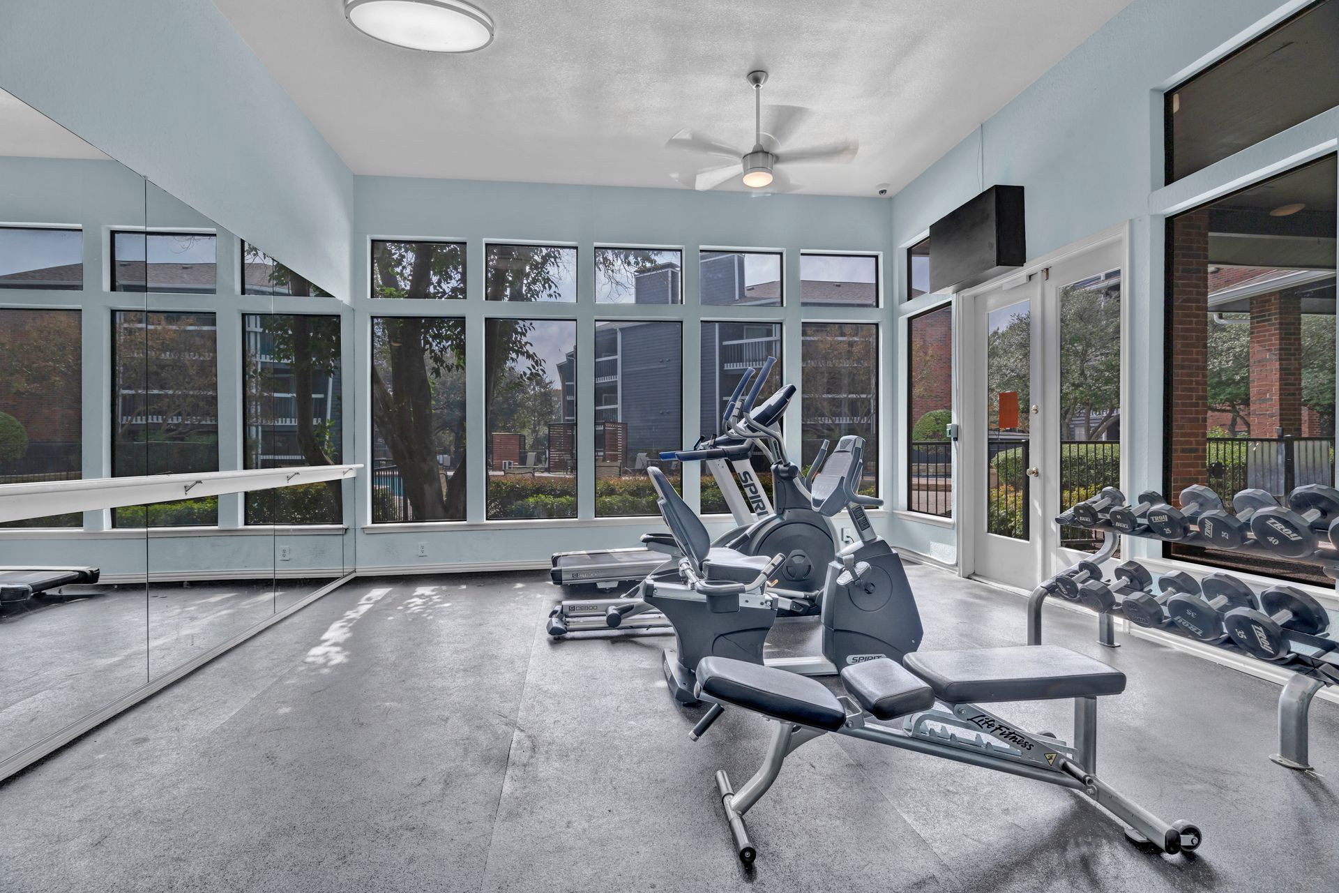 A gym with a lot of windows and a ceiling fan.