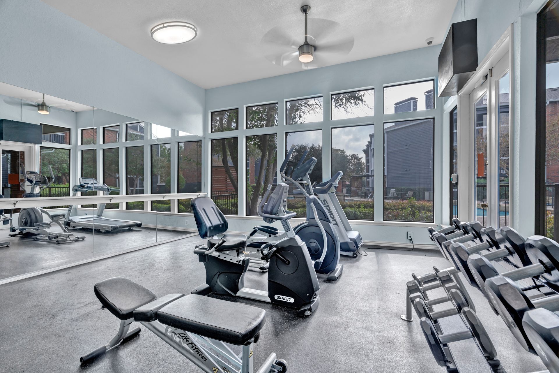 A gym with a lot of exercise equipment and a lot of windows.
