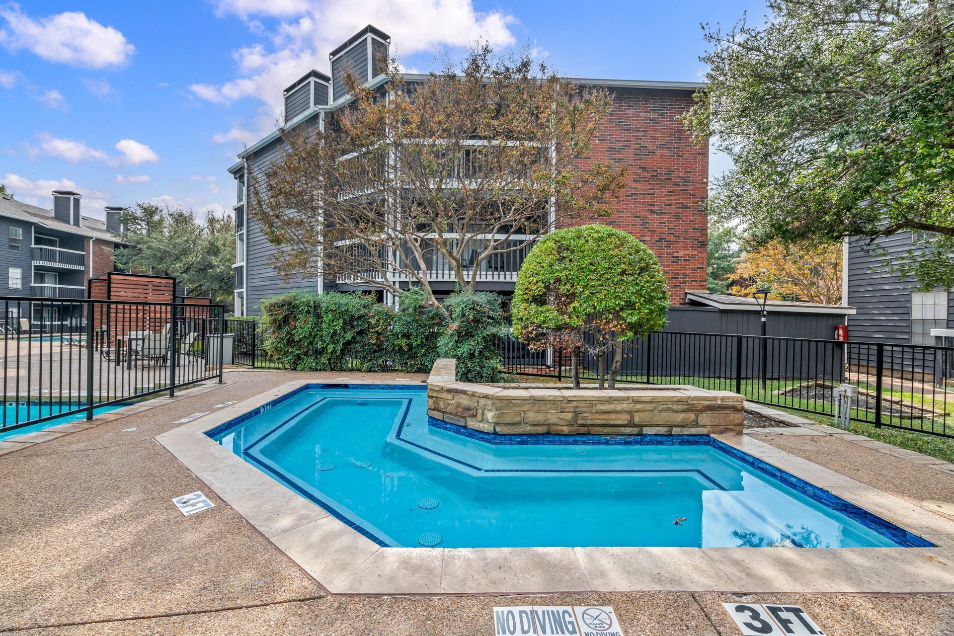 A large swimming pool is surrounded by a fence in front of a building.