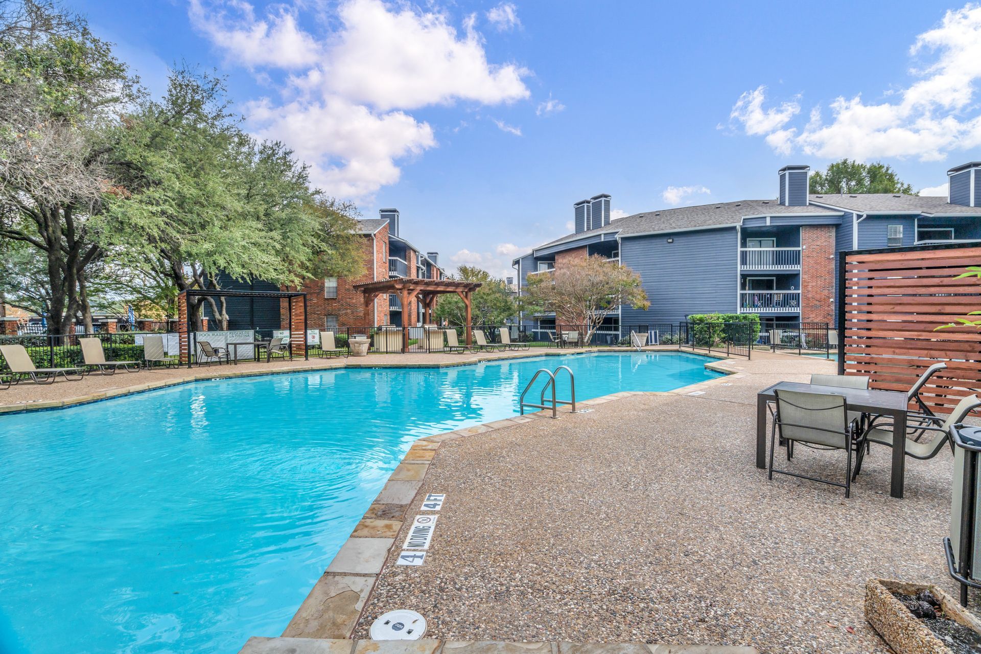 A large swimming pool surrounded by chairs and tables in front of a building.