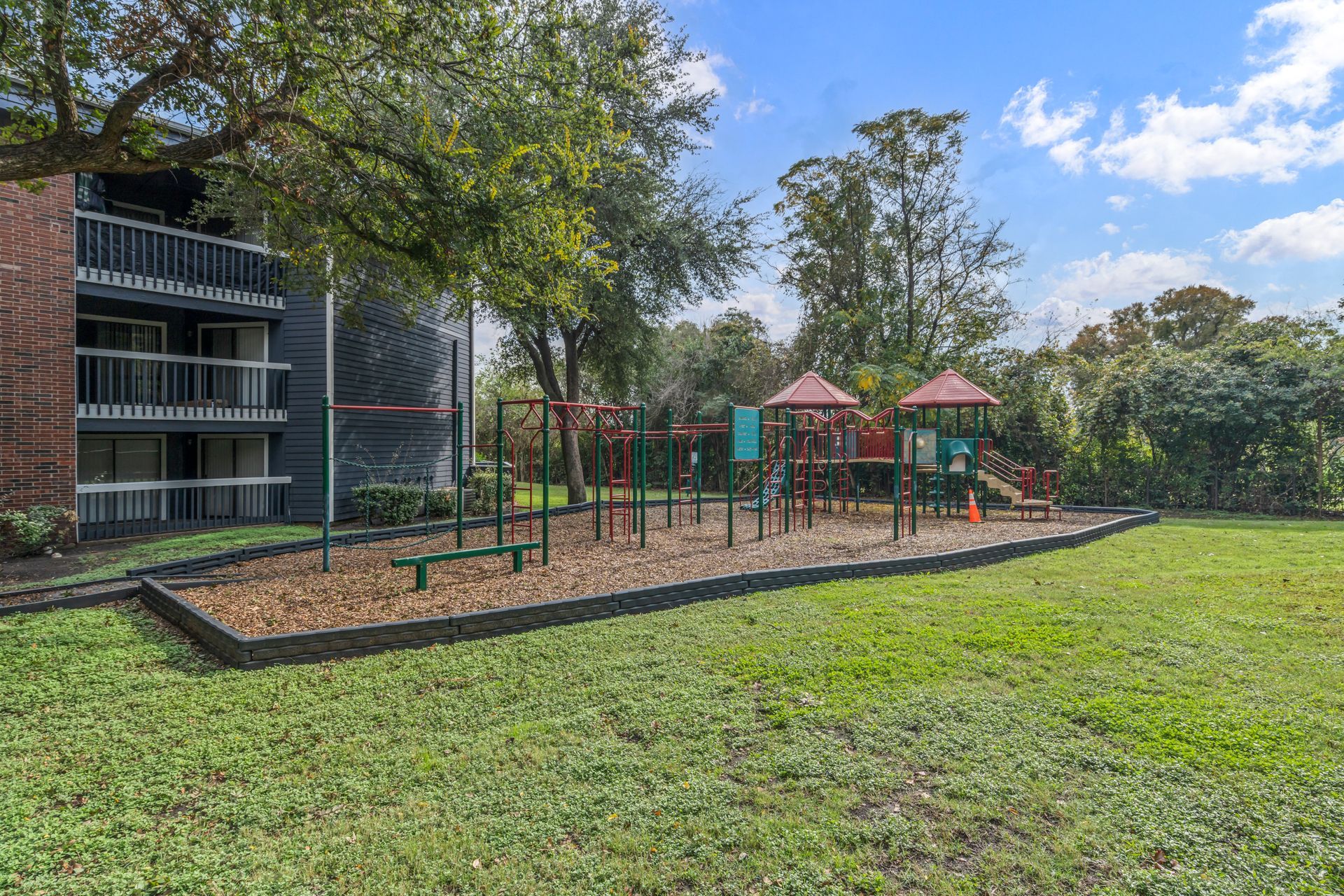 There is a playground in the middle of the grass in front of a building.