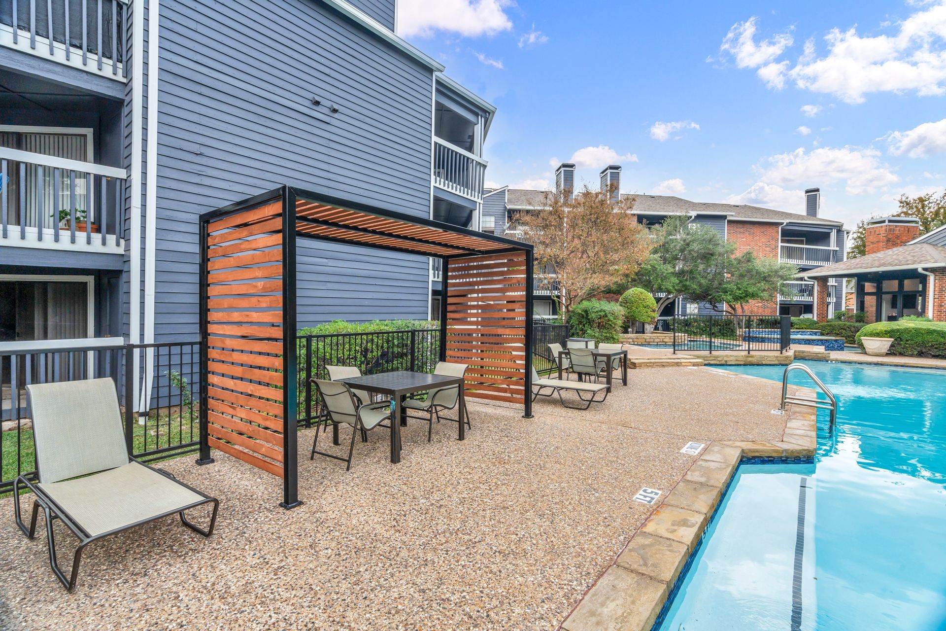 A swimming pool with a pergola and chairs in front of a building.