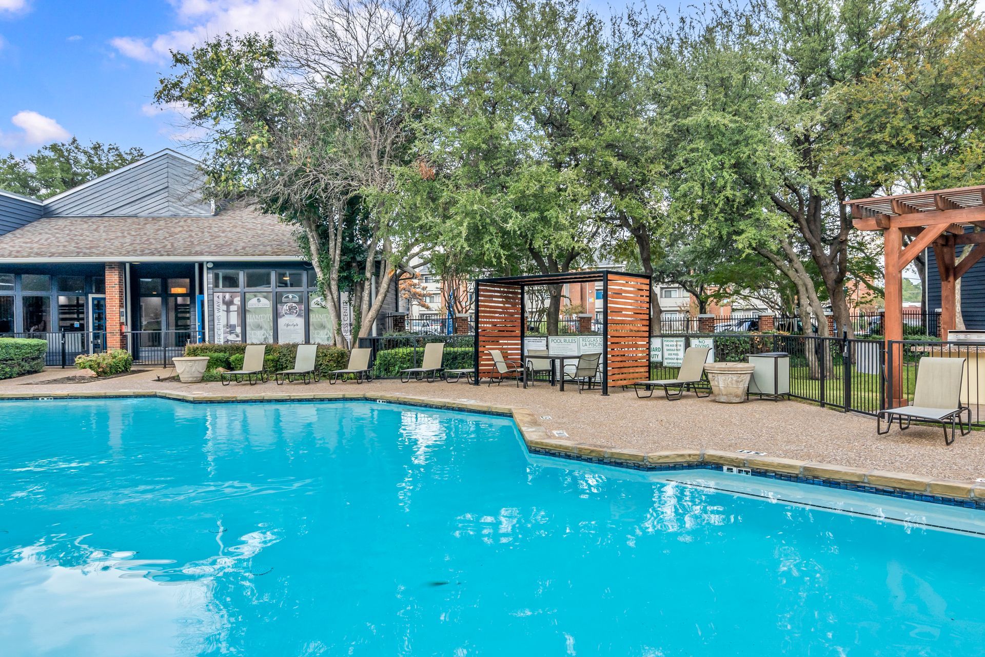 A large swimming pool surrounded by trees and chairs in front of a building.