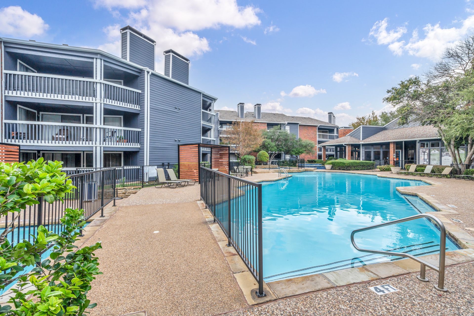 A large swimming pool is surrounded by a fence in front of a building.