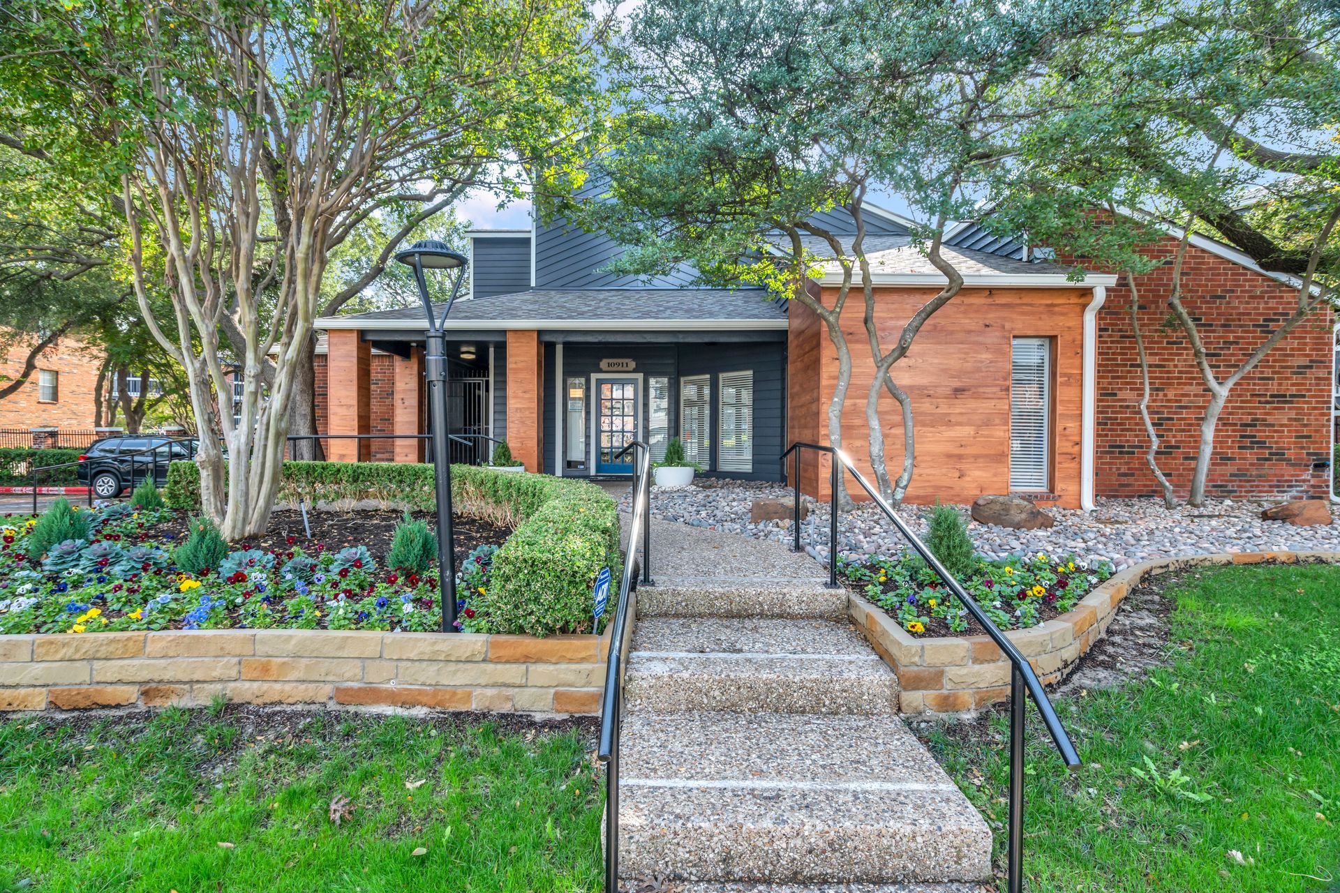 A brick house with stairs leading up to it and a lush green yard.
