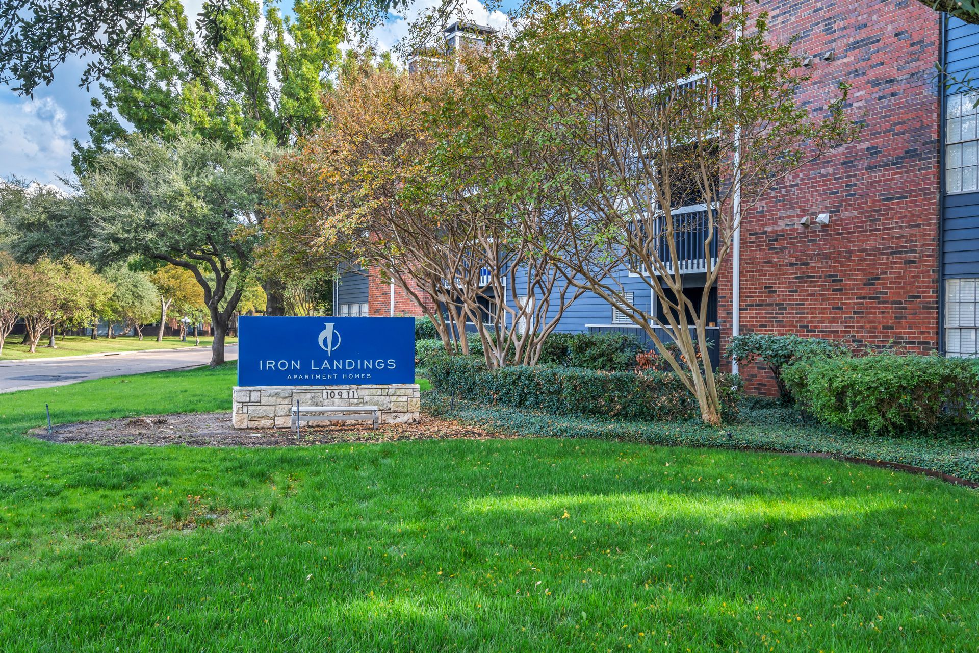 A blue sign is in the grass in front of a brick building.